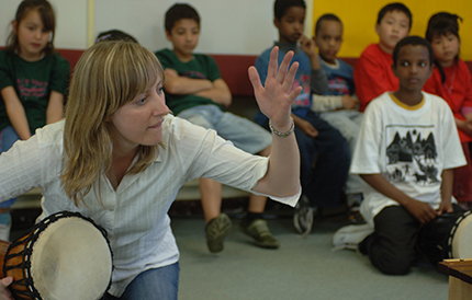 Gillian playing a drum in front of students